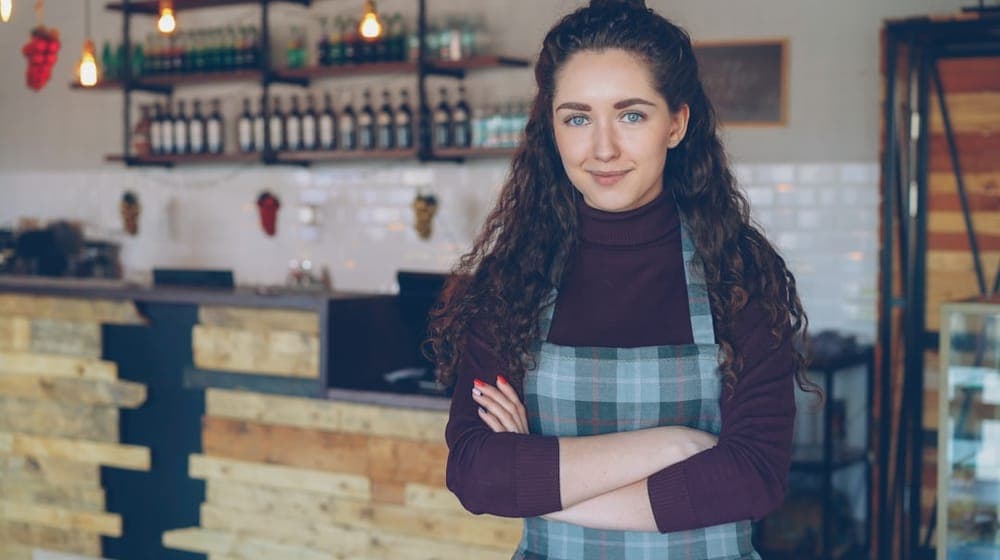 Portrait of attractive confident young woman small business owner standing in her opening coffee shop and smiling looking at camera. Coffee house interior in background.
