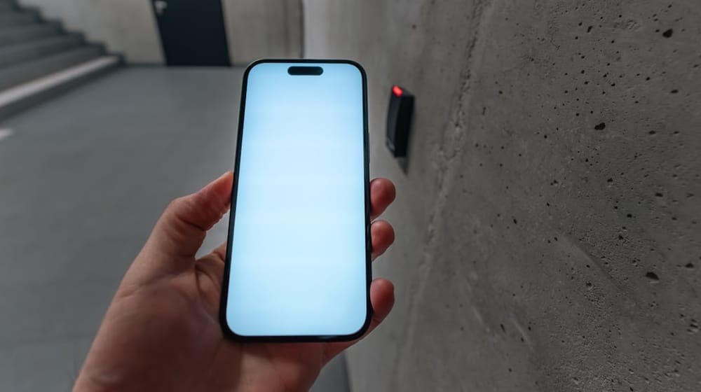 Smartphone access control reader office entry. Hand holding modern phone near wireless card terminal in concrete stairwell. Concept of digital security, NFC technology and smart access to workplace