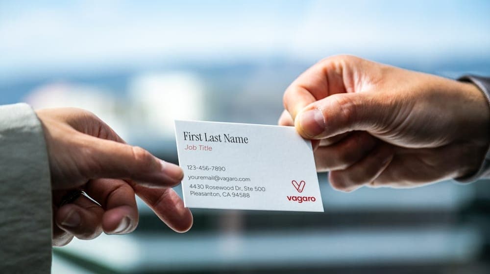 In front of an office window, the Vagaro business card is being exchanged between hands. The natural light creates depth on the back contact information which has generic information as a mockup example.